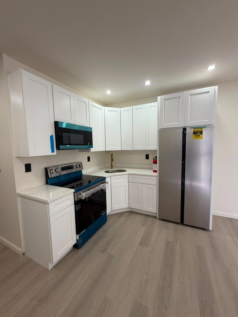 Compact white shaker kitchen with quartz counters, range and refrigerator in place