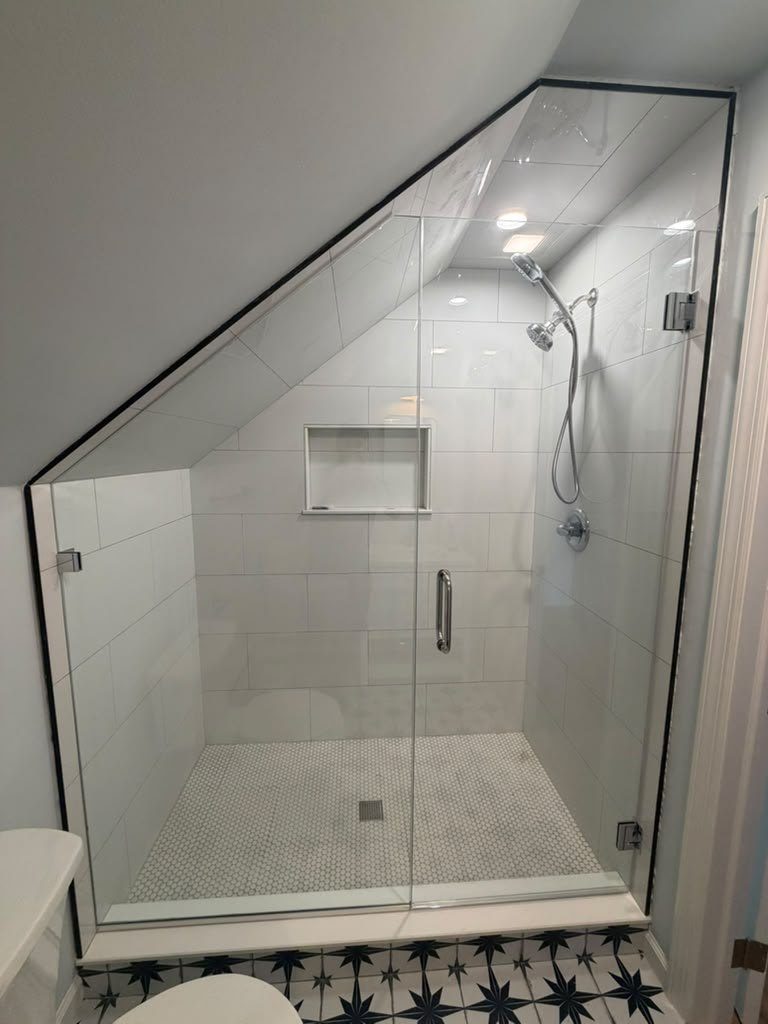 Walk-in shower lined with large marble-look stone panels under a sloped ceiling