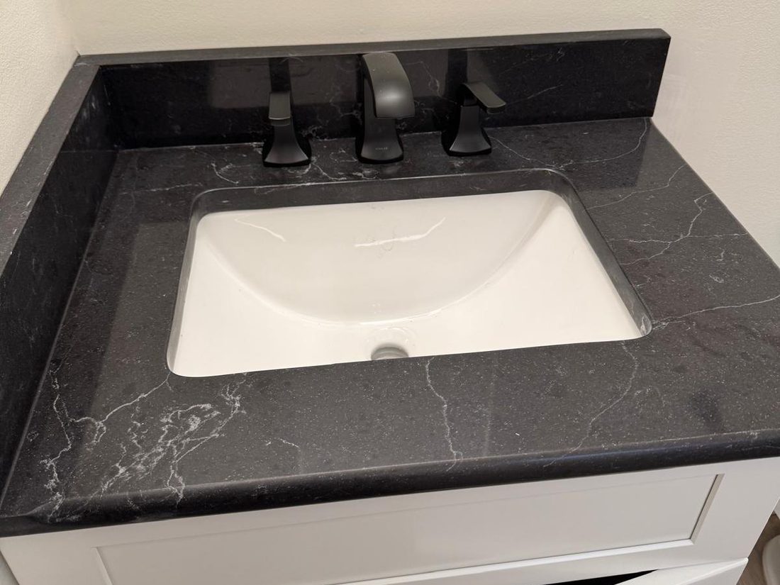 White undermount sink set into a black veined stone vanity top with a matte black faucet
