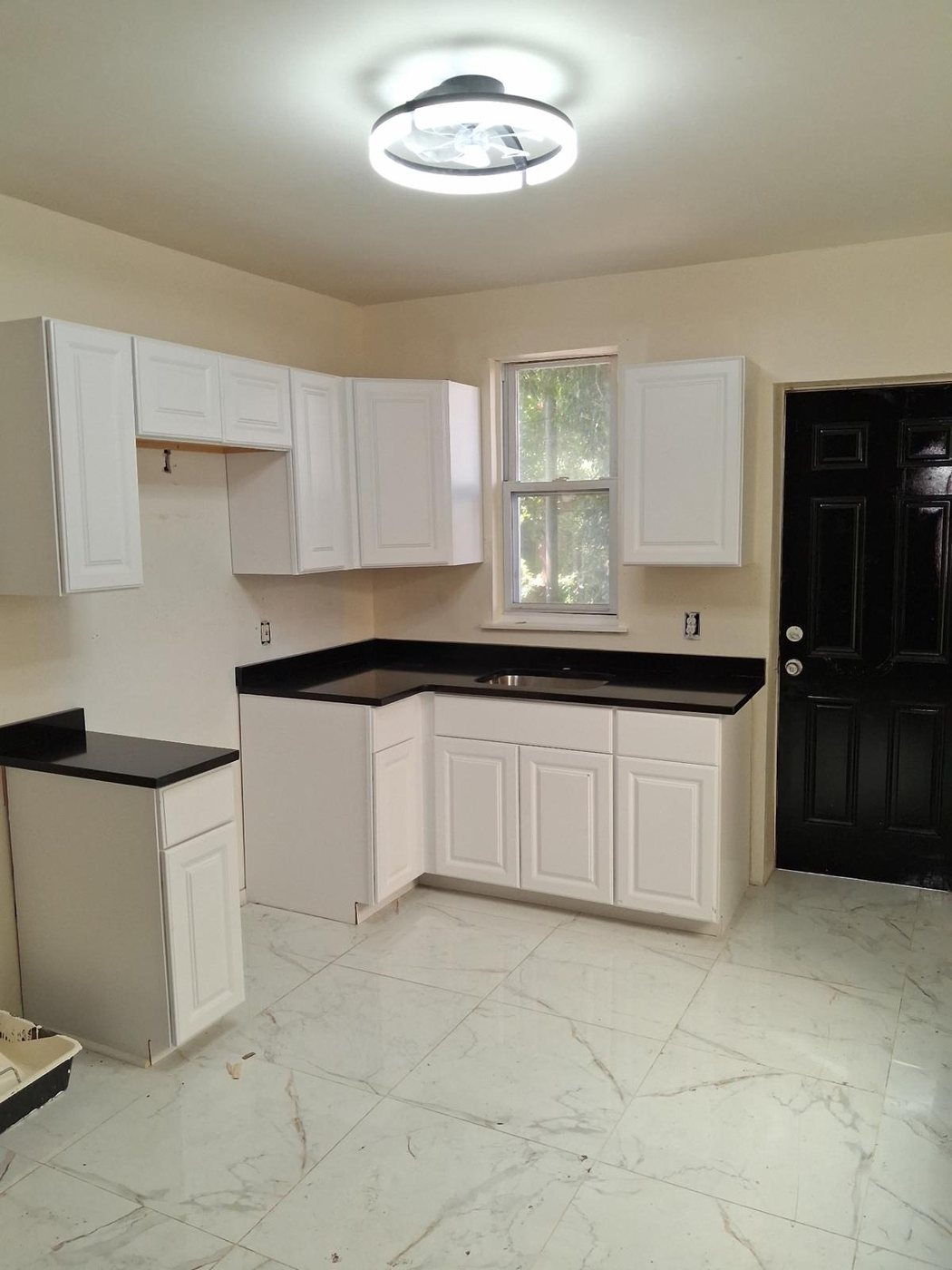 Corner run of white raised-panel cabinets finished with a black stone countertop and a stainless sink