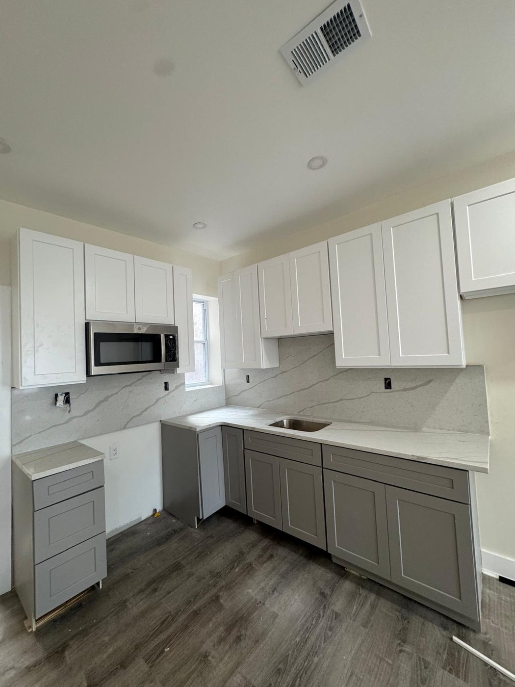 Veined white stone counter carried up the wall as a full-height backsplash, over grey base cabinets